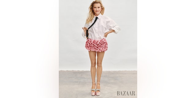 Reese Witherspoon poses wearing a pink skirt and white top