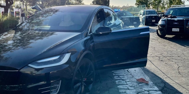 An orange Croc shoe on ground next to stolen black Tesla with door open surrounded by police