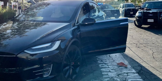 An orange Croc shoe on ground next to stolen black Tesla with door open surrounded by police