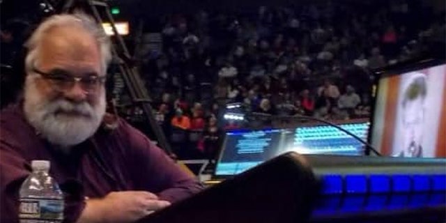 Man at concert sits in front of lighting equipment and two monitors.