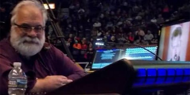 Man at concert sits in front of lighting equipment and two monitors.