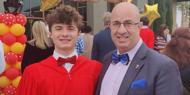 aden gilbert wearing red graduation gown stands next to his father