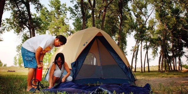 Two people inflating an air mattress outside of a tent 