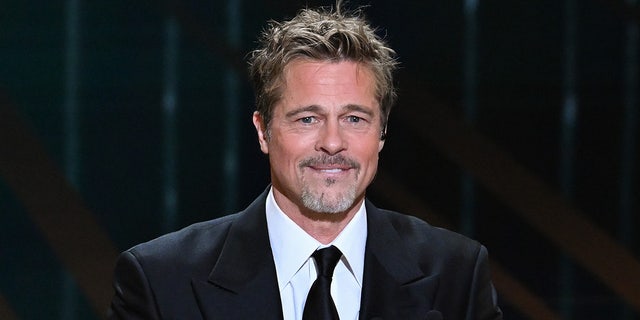 Brad Pitt bites his lower lip and smiles in a black suit
