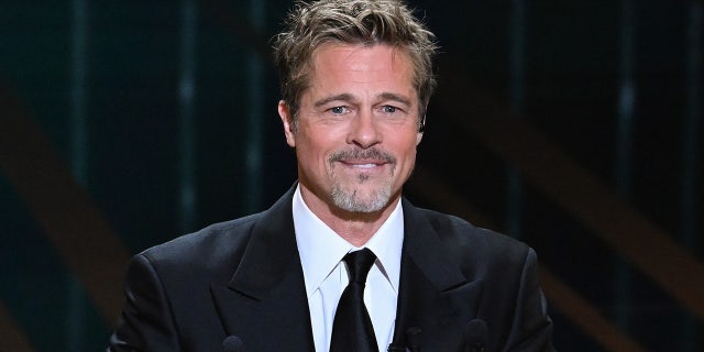 Brad Pitt bites his lower lip and smiles in a black suit