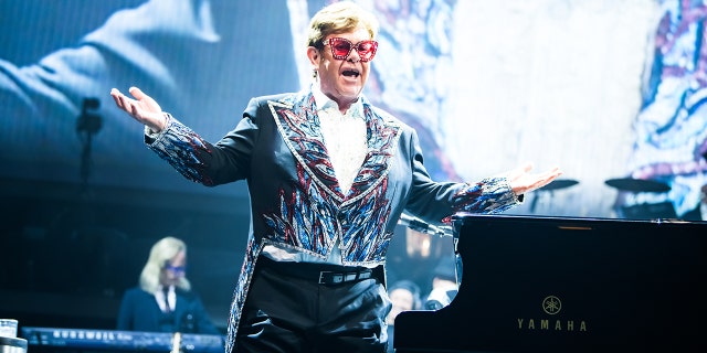 Elton John Stands on stage wearing sunglasses