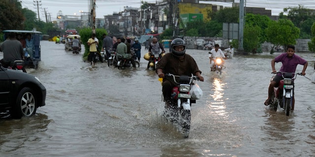 Motorcyclists drive through a flooded roads