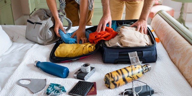Two people pack luggage on a bed.