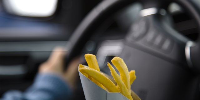 Person holds French fry container while driving.