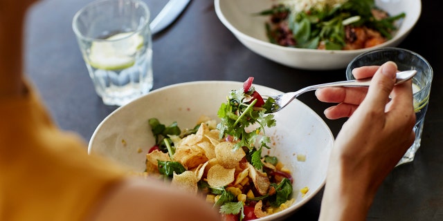 Woman eats healthy meal across from somone.