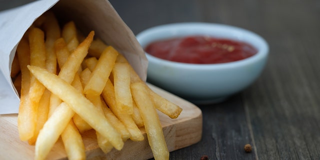 Container of French fries next to bowl of ketchup.