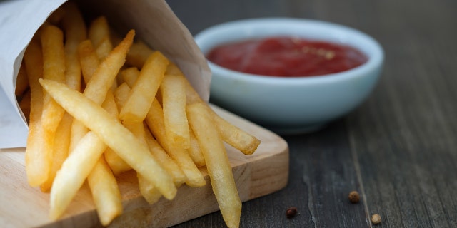 Container of French fries next to bowl of ketchup.