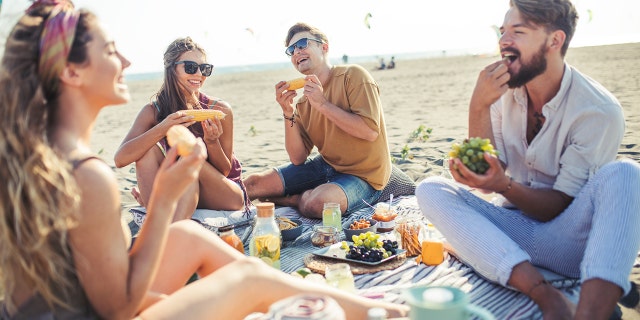 People eat while on a beach picnic.