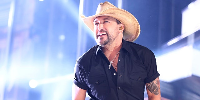 Jason Aldean looks up in a blue shirt and tan cowboy hat while performing