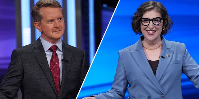 Ken Jennings in a dark suit and red tie looks to contestants while on Jeopardy! split Mayim Bialik in a blue jacket behind a podium on "Jeopardy!"