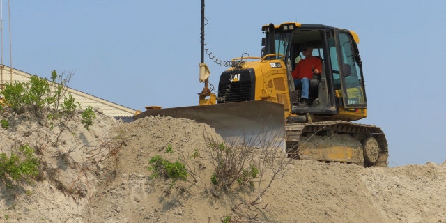 Bulldozer operator repairing eroded dunes in North Wildwood, New Jersey