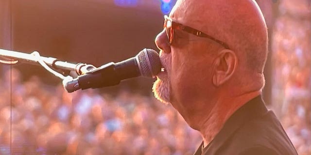 Billy Joel sings into a microphone while performing on stage