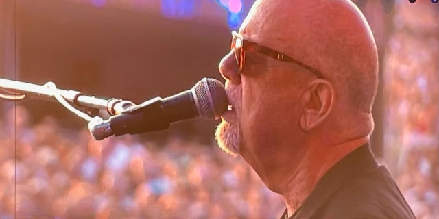 Billy Joel sings into a microphone while performing on stage