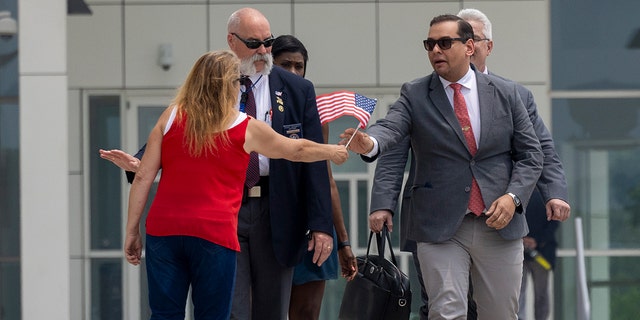 Rep. George Santos (red tie) is presented with a miniature American flag as he departs federal court