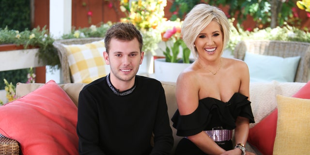 Chase and Savannah Chrisley smile and sit on the couch for a photo
