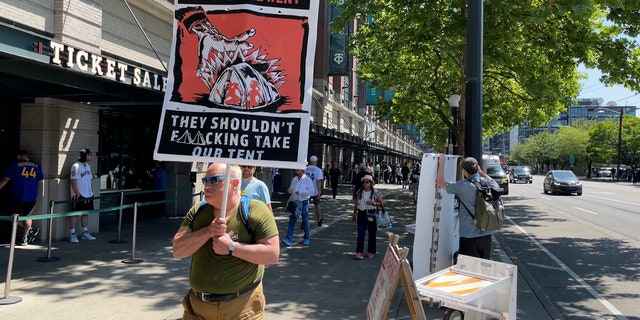 Man holds sign against homeless sweeps