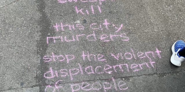 Chalk writing says "sweeps kill, this city murders, stop the violent displacement of people" in Seattle
