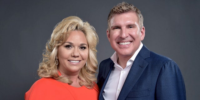 Julie Chrisley in an orangey dress smiles next to husband Todd Chrisley in a navy suit