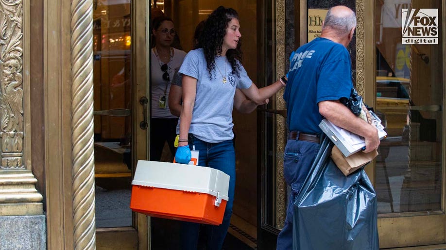 A Suffolk County Crime Lab detective carries items out of 385 Fifth Avenue