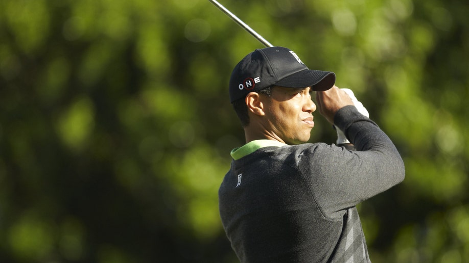 Tiger Woods playing golf in a black hat and jacket