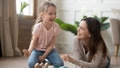 Happy family mom baby sitter and little kid daughter laughing playing with wooden blocks sit of warm floor, joyful mother having fun with child girl enjoy funny activity laughter at home together