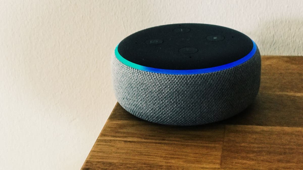 A gray Amazon Echo device on a dark wooden table