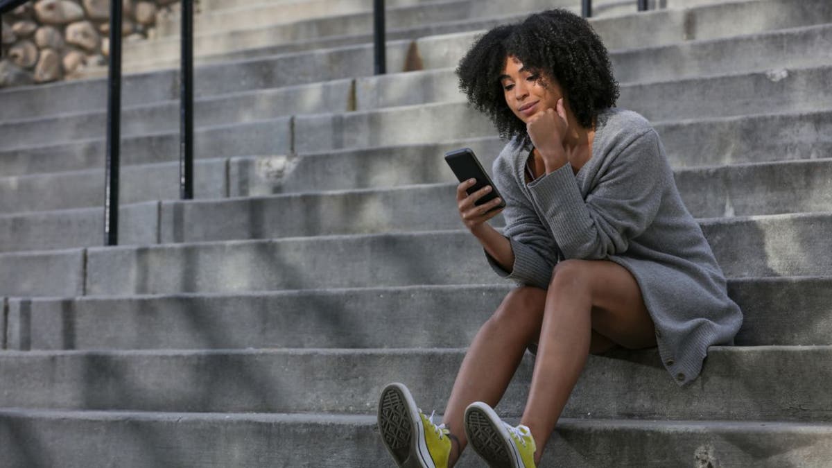 Woman sits on building steps and holds her phone