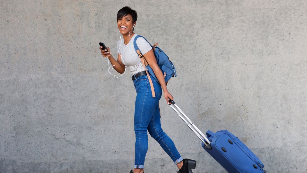 Woman walking with her phone and luggage.