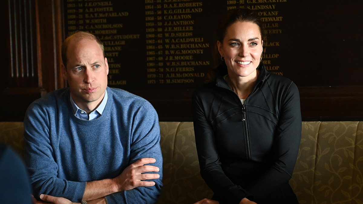 Prince William in a baby blue swearter sitting next to Kate Middleton in a hunter green jacket