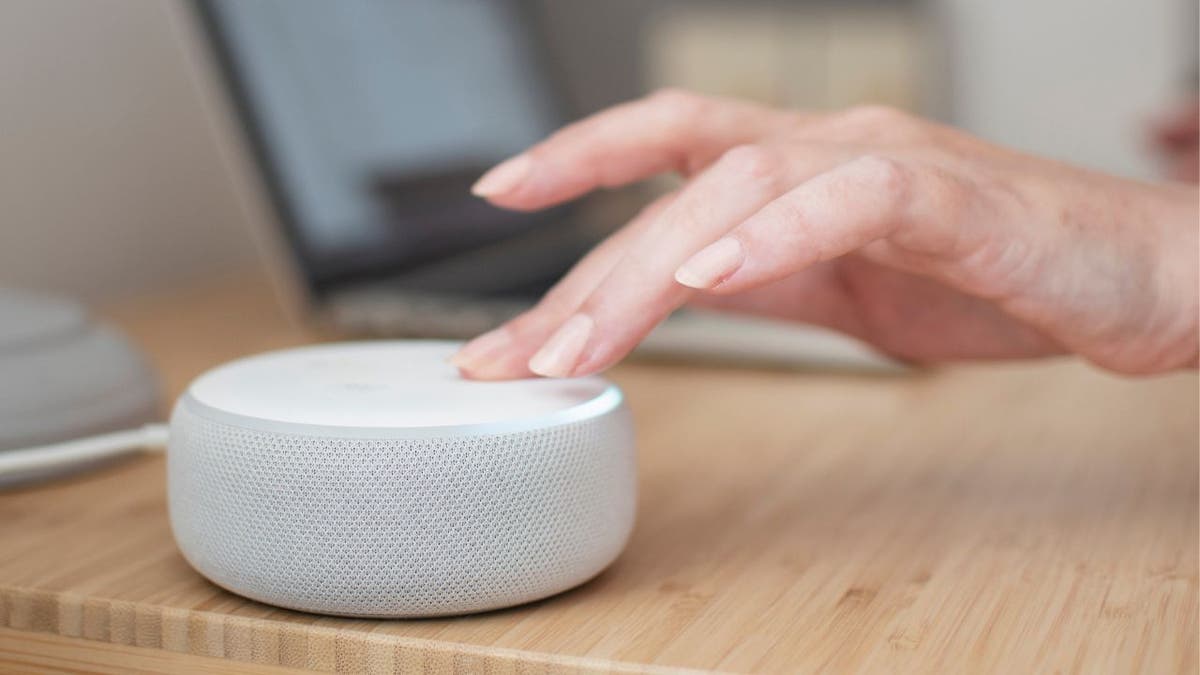 White Amazon Alexa device on a light wooden table with a hand touching the device