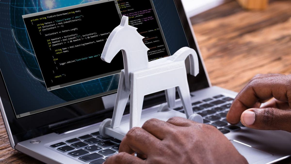 White mini Trojan horse model placed on the keyboard of a laptop with data on the screen