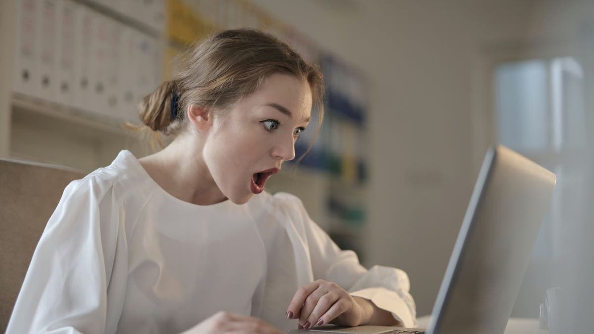 Woman looking at her laptop shocked at finding out that she has been scammed.