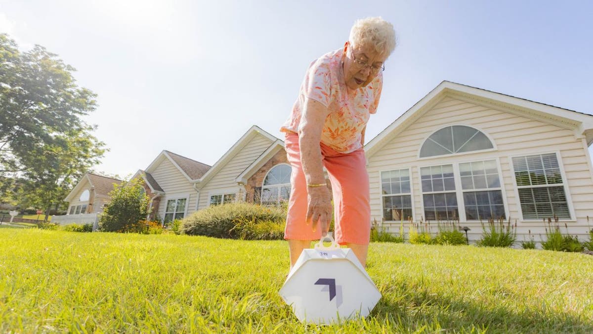 Susie is bending down to pick up her Wing delivery service order in her front yard