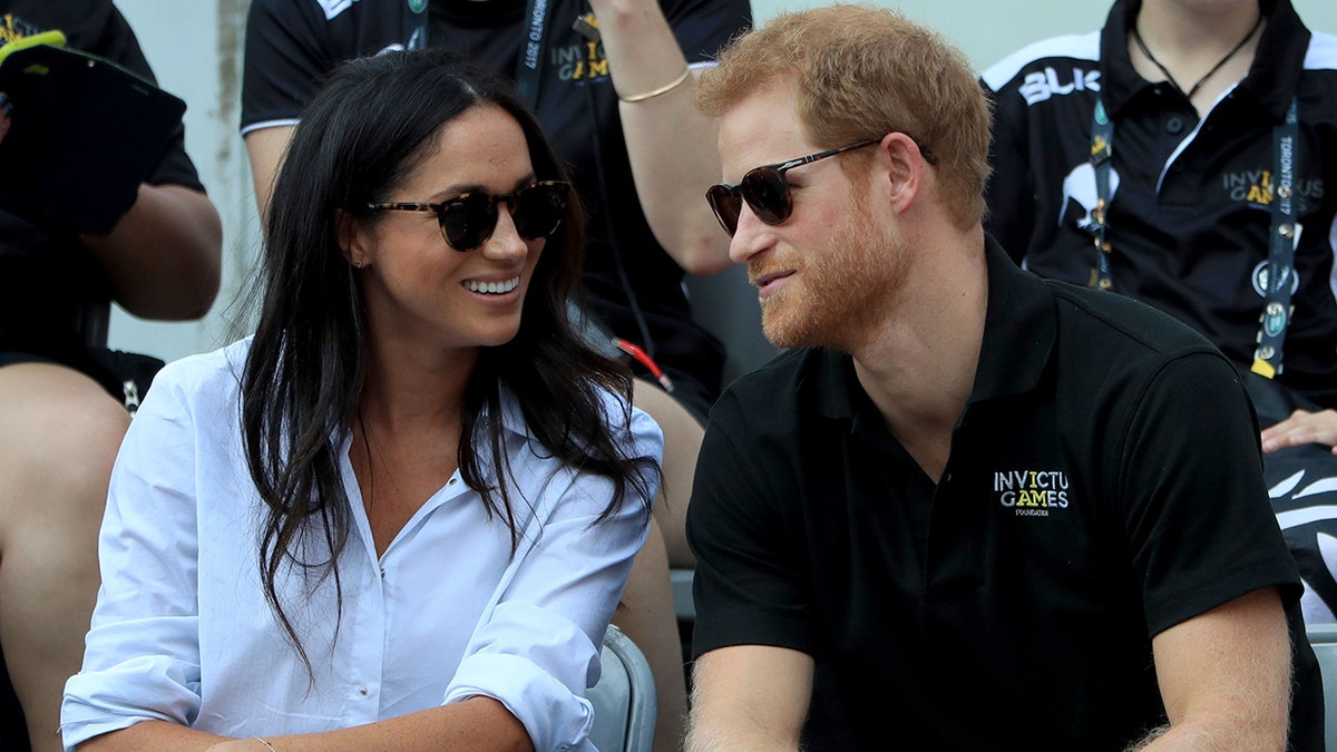 Meghan Markle in a white shirt and sunglasses smiles at Prince Harry in a black polo at the Invictus Games in Toronto