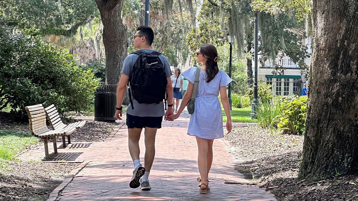 couple holds hands walking through park