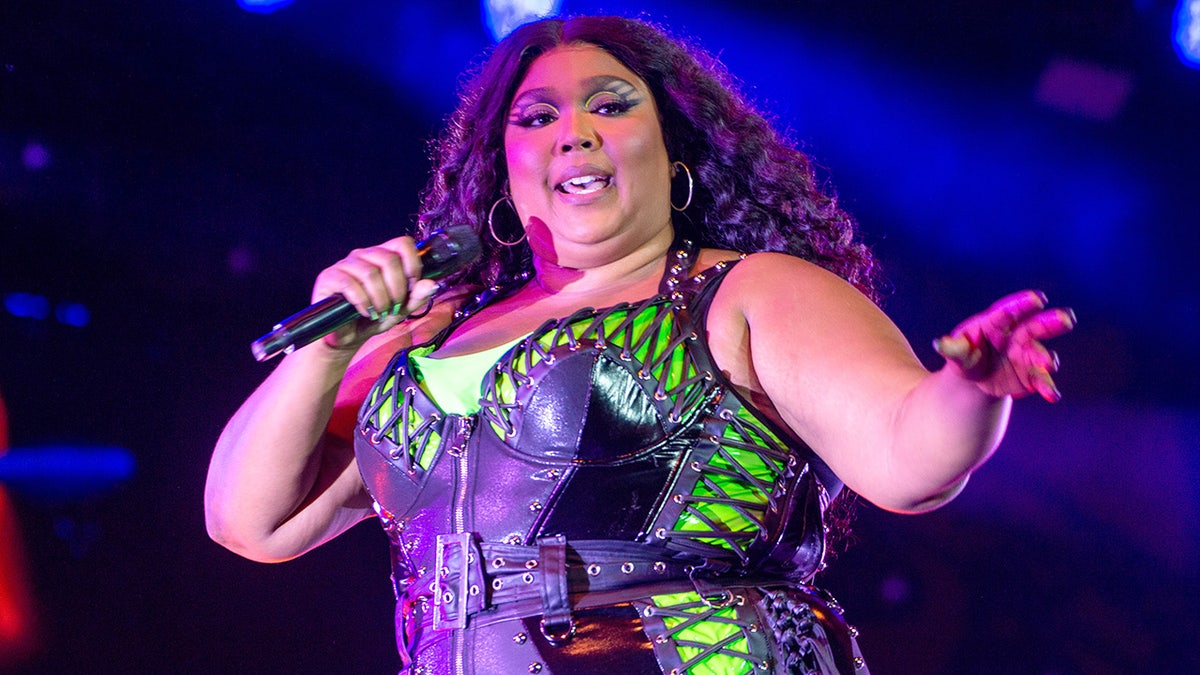 Lizzo in a neon green top with a black bodysuit over it sings on stage in Denmark
