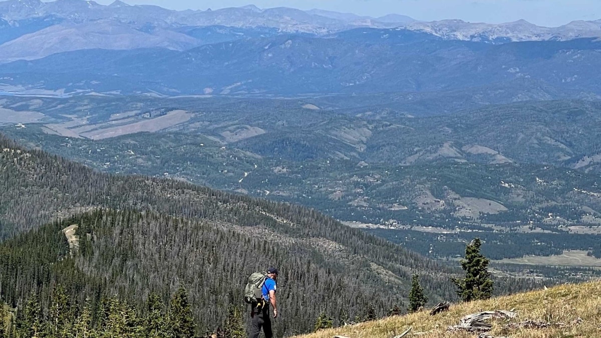 A man and a dog search on a trail with mountains in the background