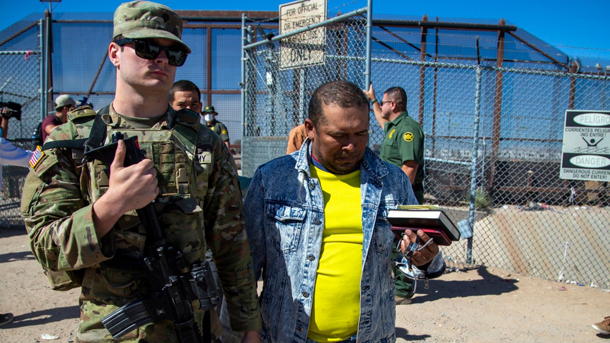 Migrants are escorted by a U.S. Army soldier after entering into El Paso, Texas from Ciudad Juarez, Mexico to be processed by immigration authorities, May 10, 2023. 