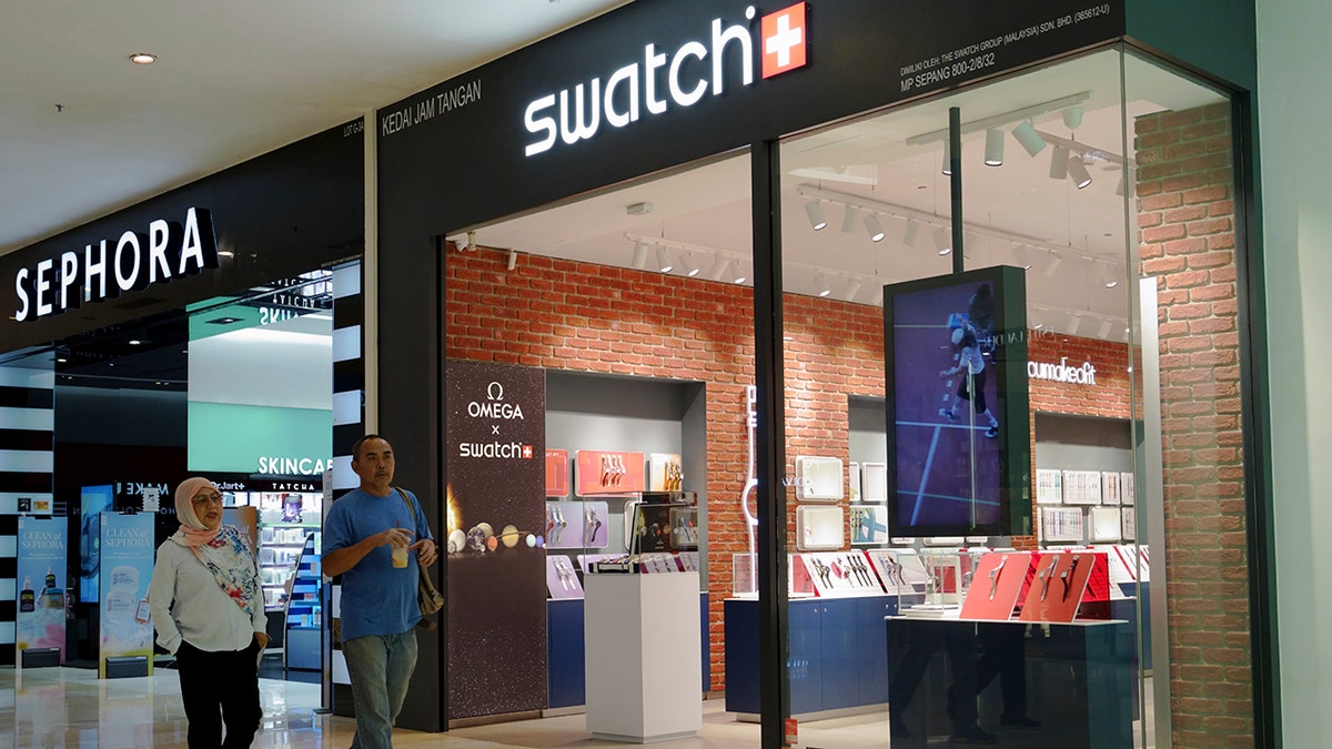 A couple walks past a Swatch outlet store in Putrajaya, Malaysia, on Aug. 10, 2023. 