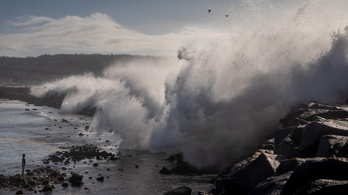 A boy plays in the water as giant waves crash over the breakwall of Redondo Beach
