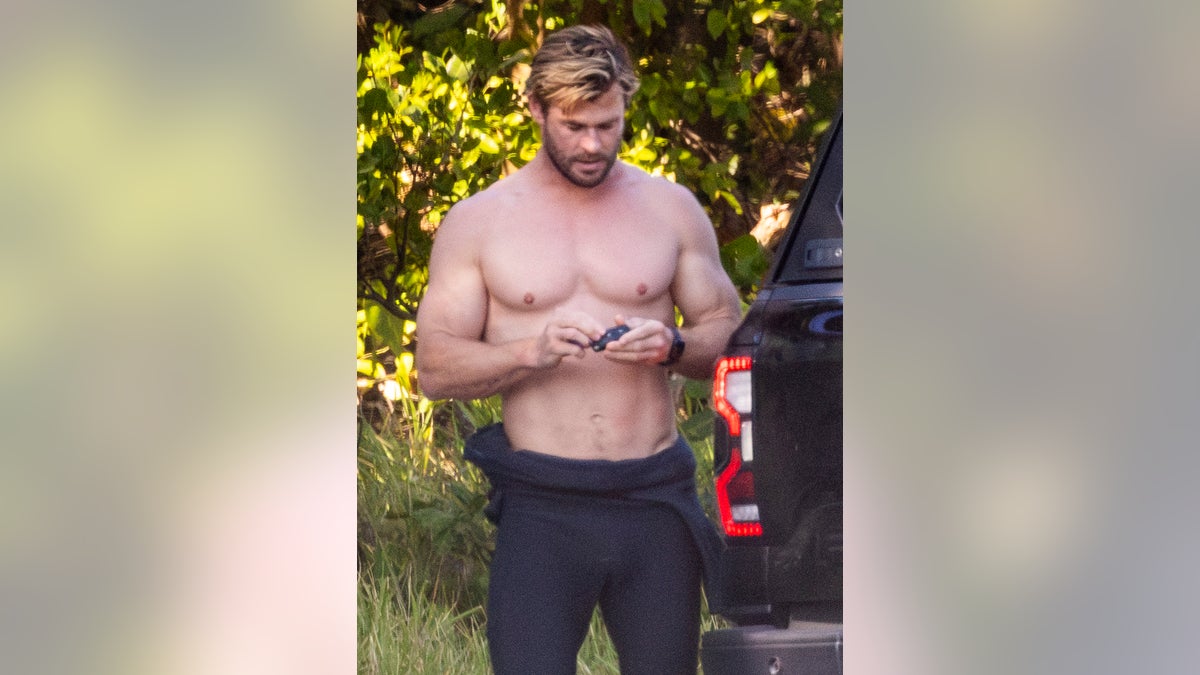 chris hemsworth shirtless in wetsuit looking at phone