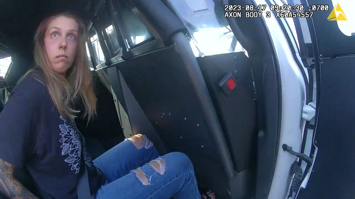 woman stares at camera from police cruiser.