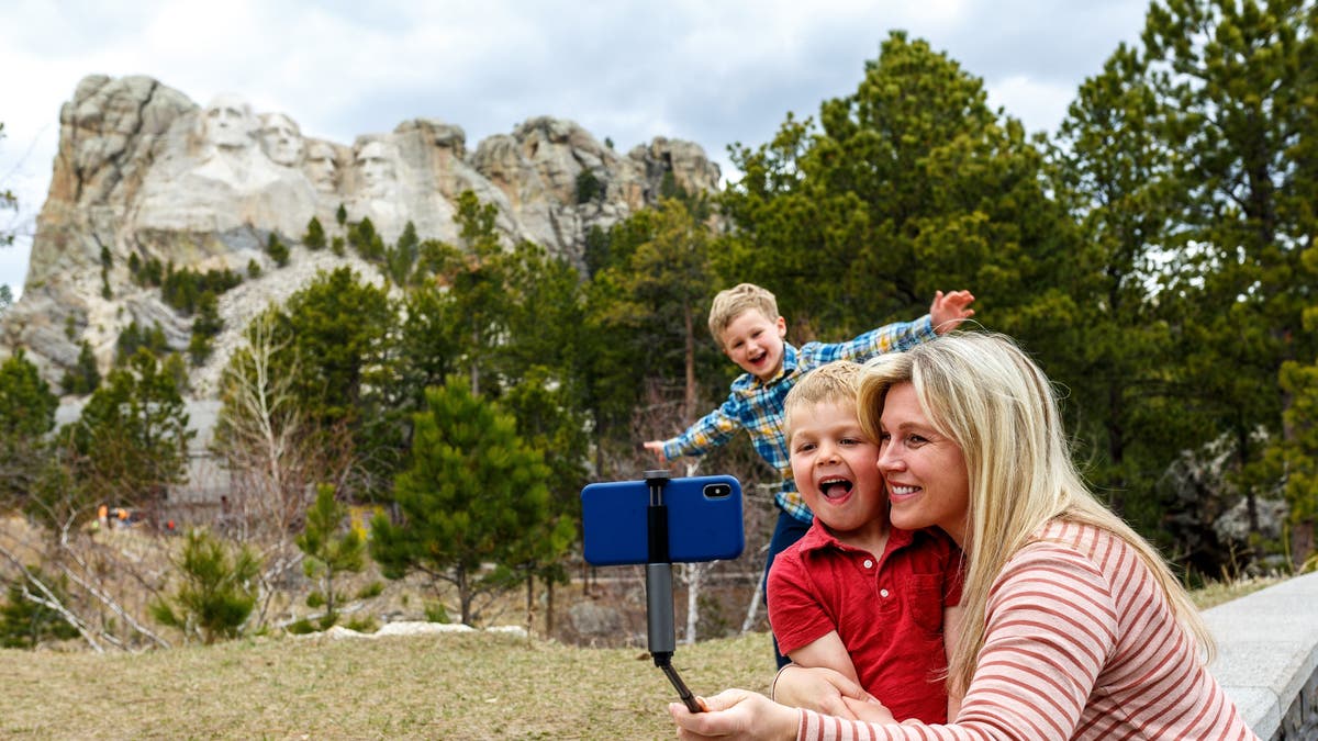 A mother poses for a selfie with her two sons with Mt. Rushmore in the background