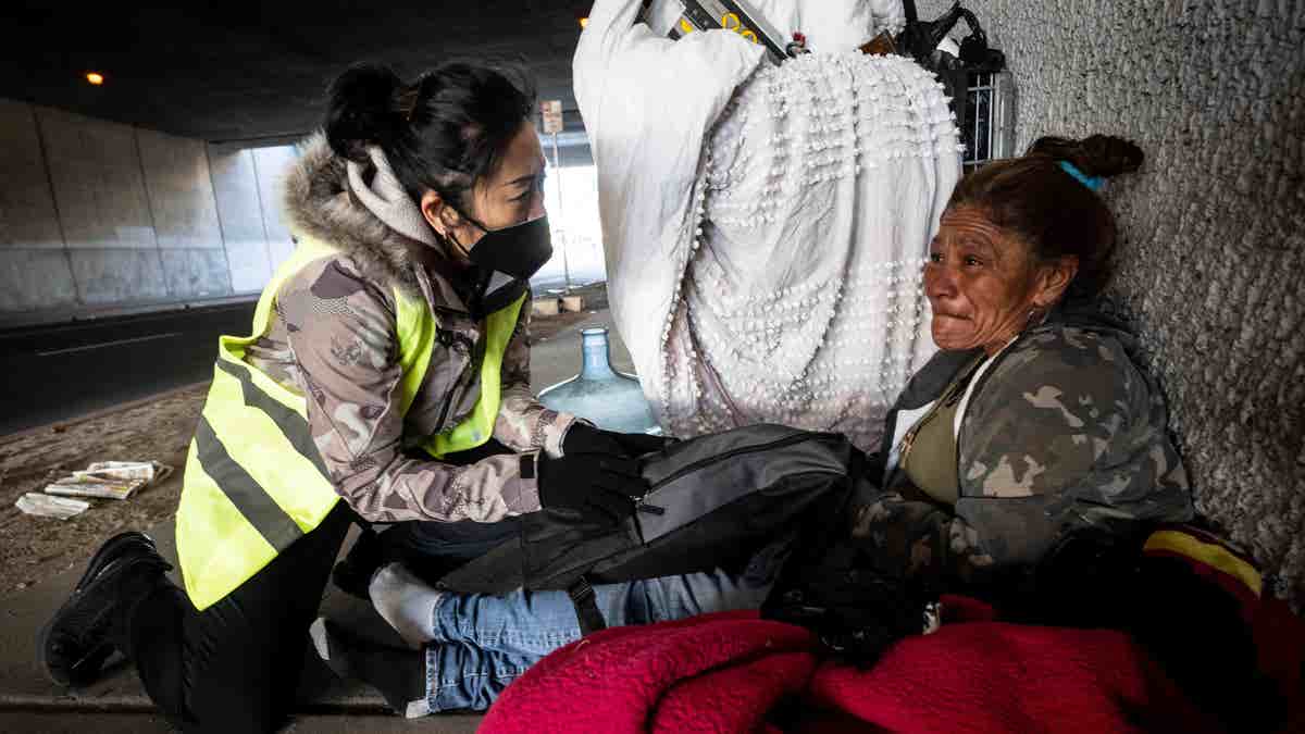 San Bernardino Mayor handing homeless woman under bridge a care package.