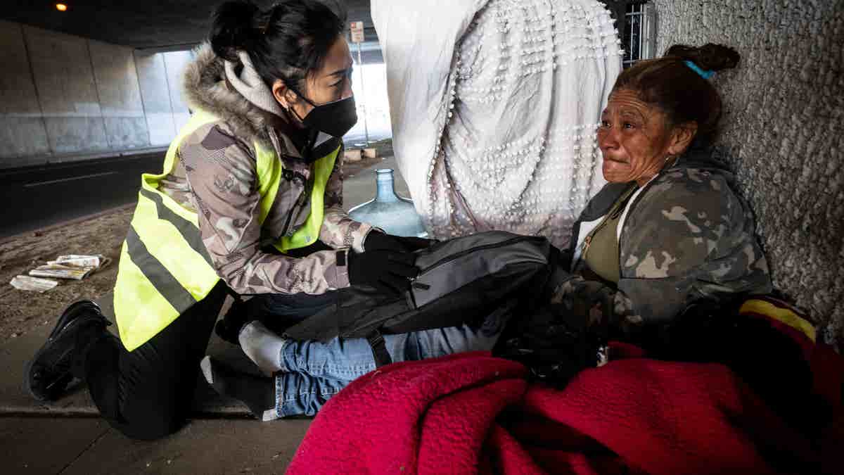 San Bernardino Mayor handing homeless woman under bridge a care package.